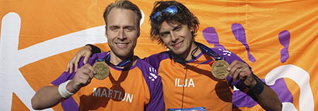 twee KiKa deelnemers in KiKa shirt, met medaille en met de oranje KiKa vlag op de achtergrond